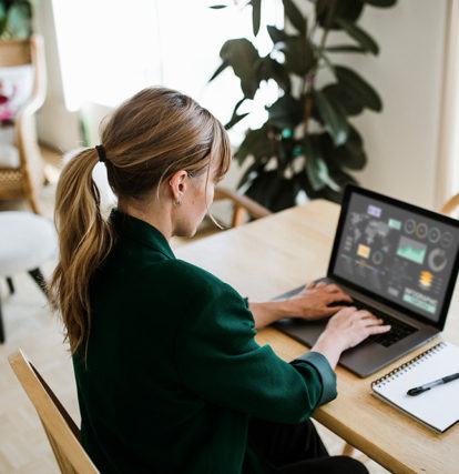 a woman sitting at a table and looking at graph data on a laptop computer