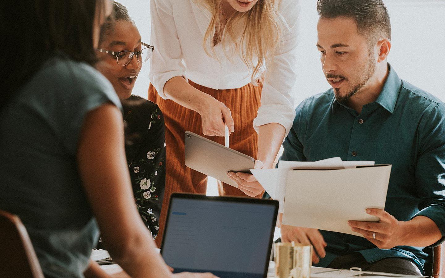 a business team working through a meeting on their laptop, tablet and documents