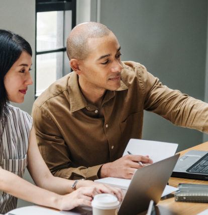 a man and a woman smiling and working together on laptop computers