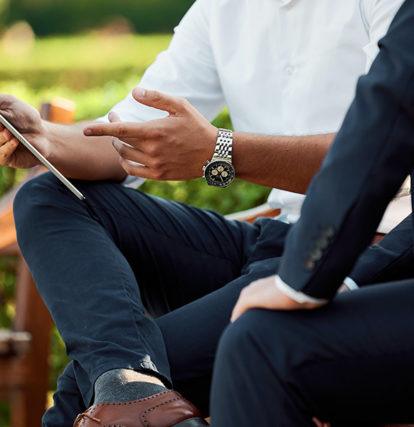 two business men sit on outdoor benches working on tablet